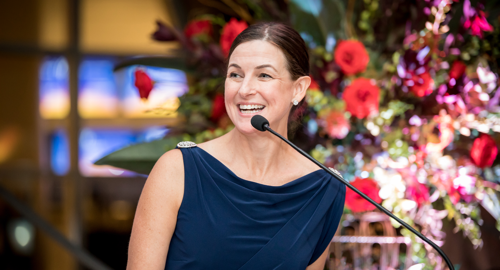 Fernbank's President and CEO, Jennifer Grant Warner, speaking at a podium, with a large floral arrangement behind her.